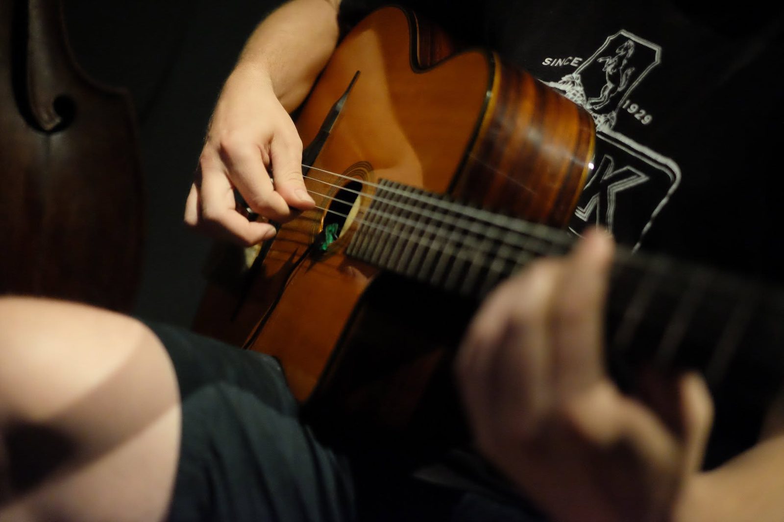 Close-up of a right hand picking a Selmer-style guitar beside a double bass