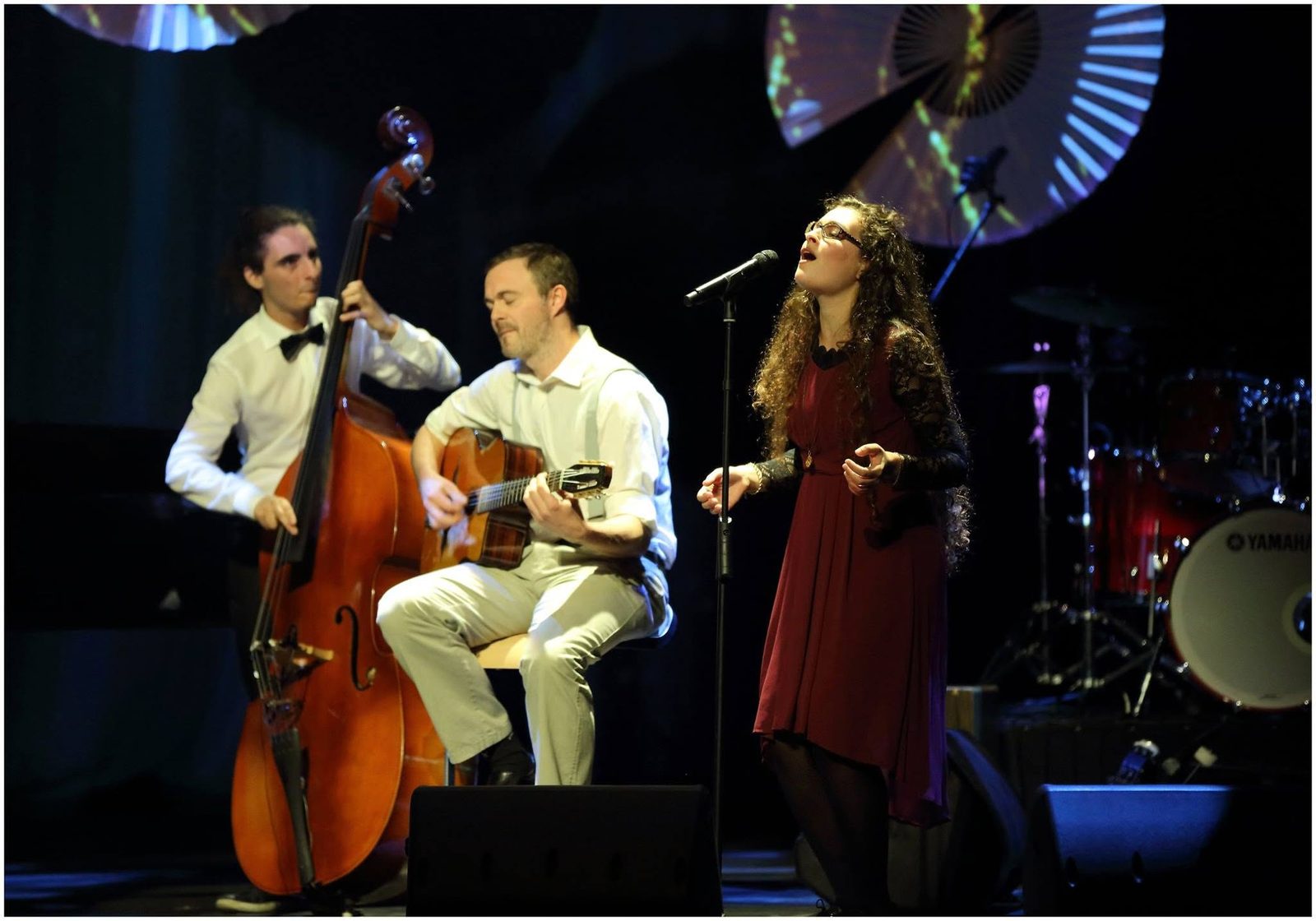 Josh playing gypsy jazz guitar on stage with a double bassist and a singer