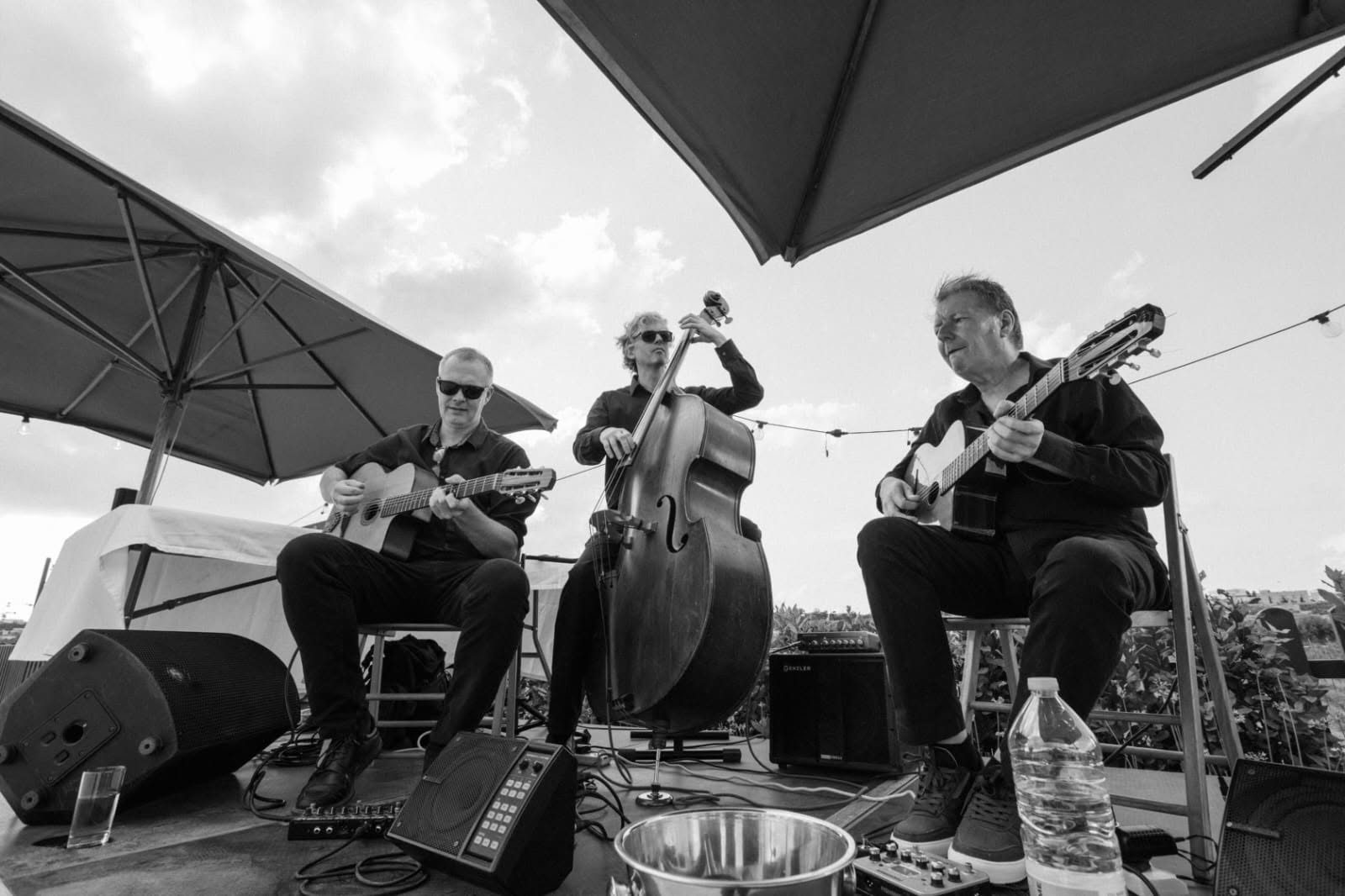 A gypsy jazz trio with two guitars and double bass playing outdoors under parasols